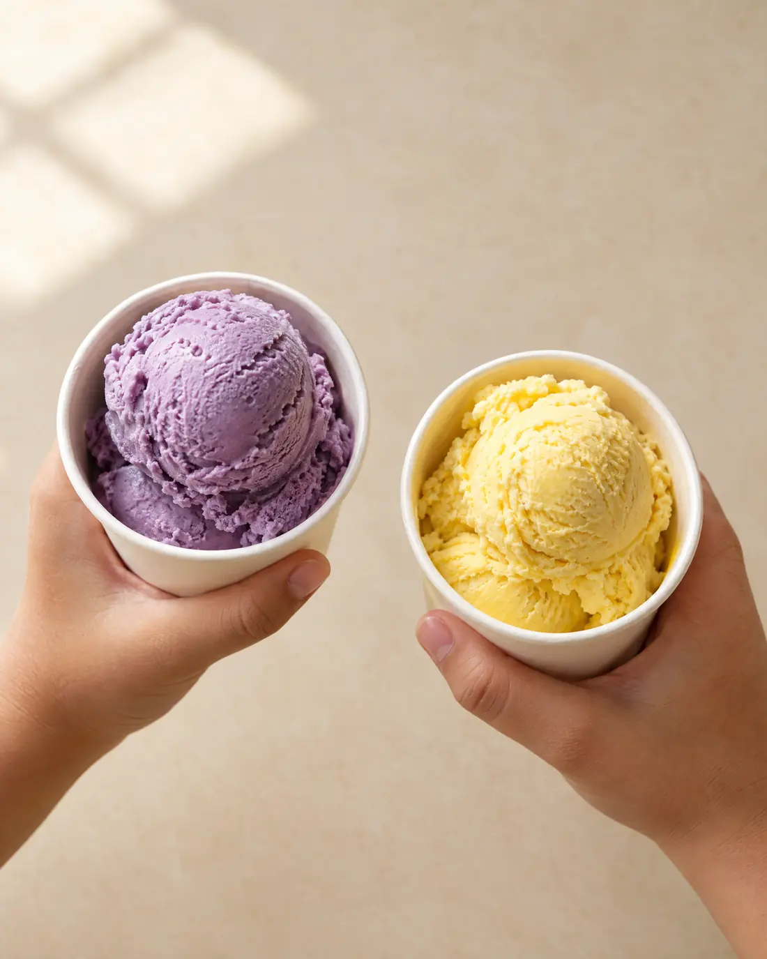 Zwei Kinderhände halten Becher mit violettem und gelbem Eis